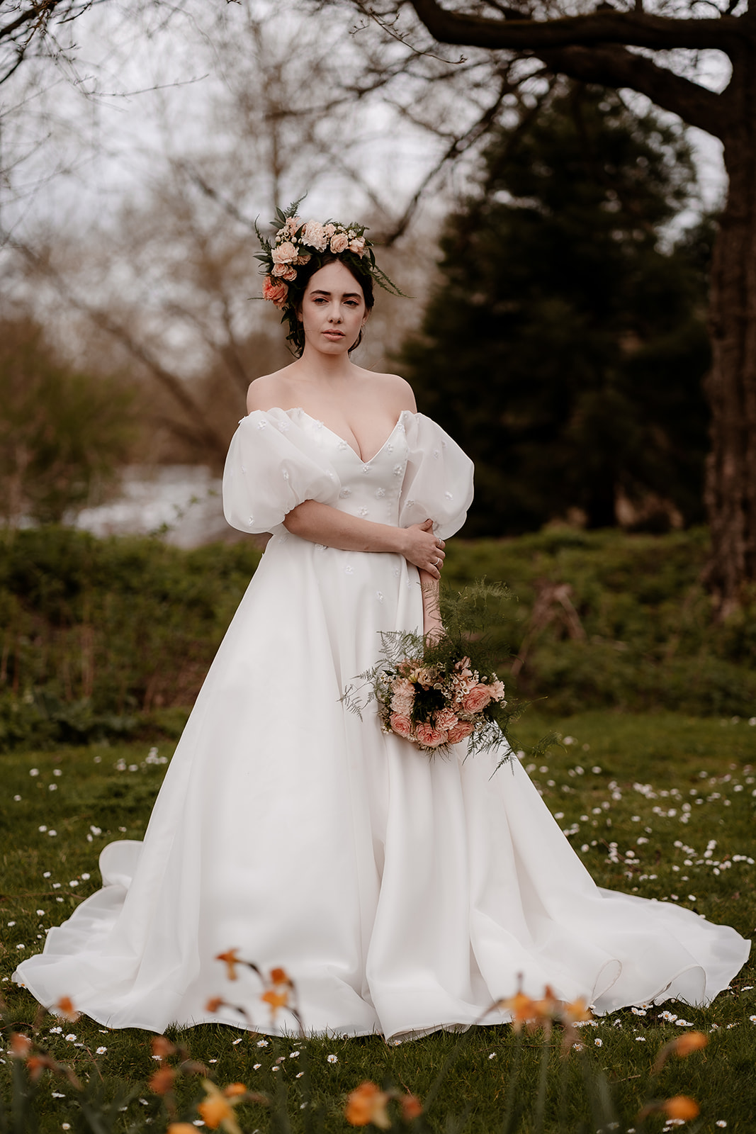 Bride wearing a flower crown and dress with puff sleeves stands among the daffodils at Mapledhurham House