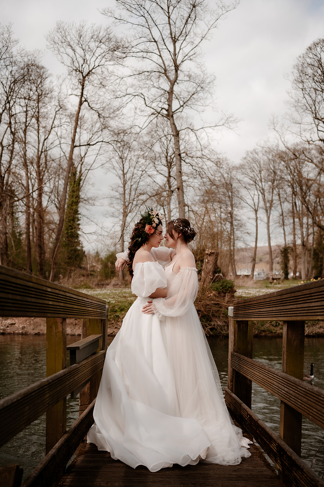Two brides stand together on a bridge at Mapledurham House wedding venue