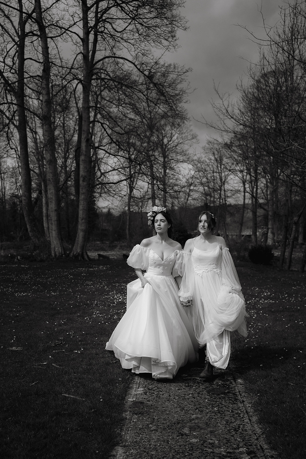 Black and white photo of two brides walking together across the grounds of Mapledurham House wedding venue