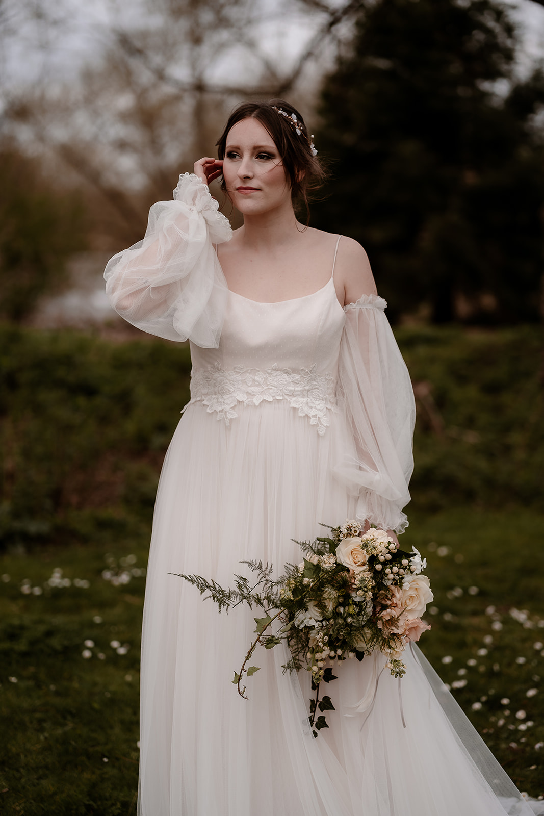 Bride in a tulle wedding dress with sheer sleeves stands holding her bouquet at Mapledurham House wedding venue