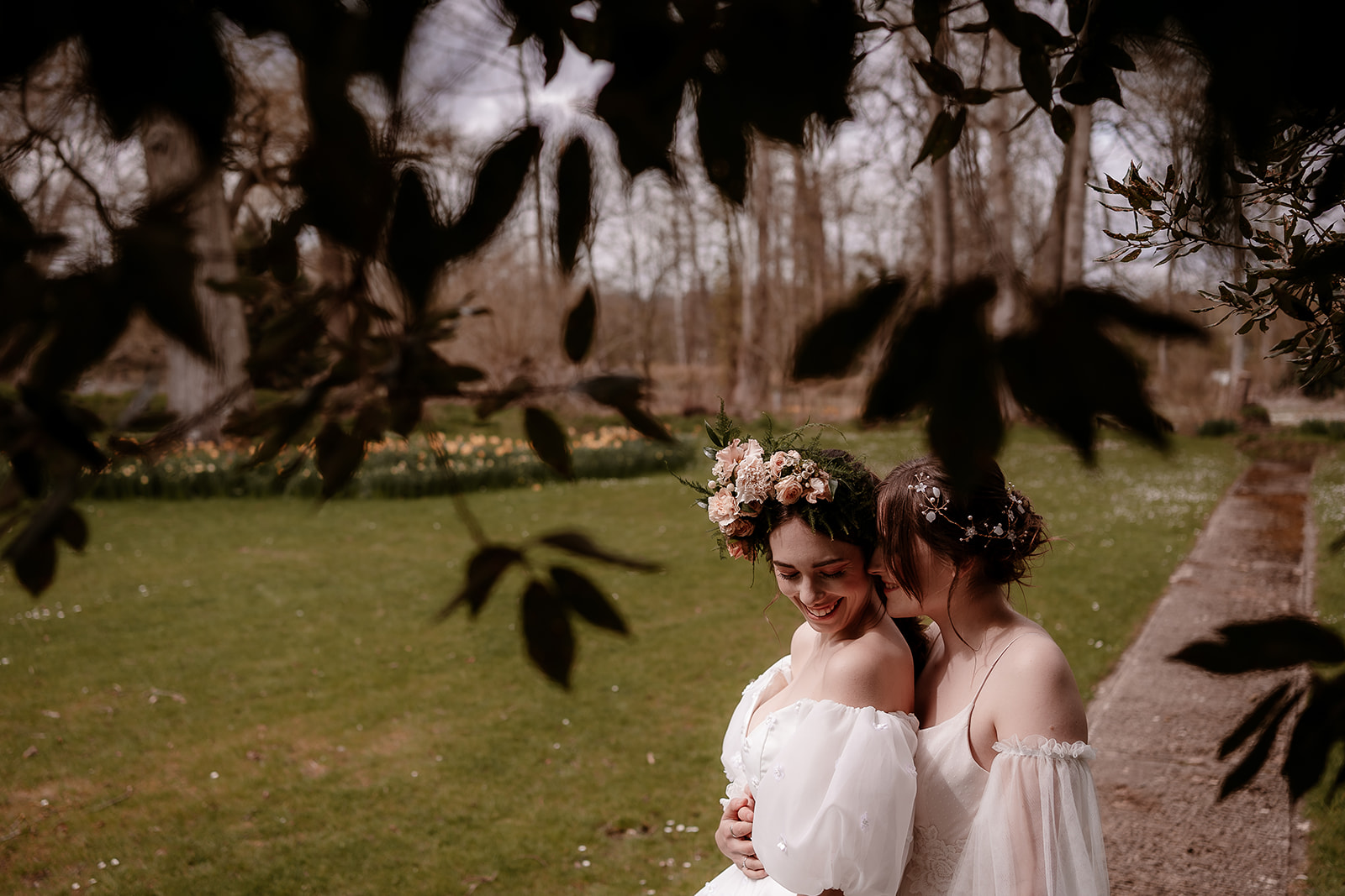 two brides snuggle together on the grounds of Mapledurham House wedding venue in the spring sunshine