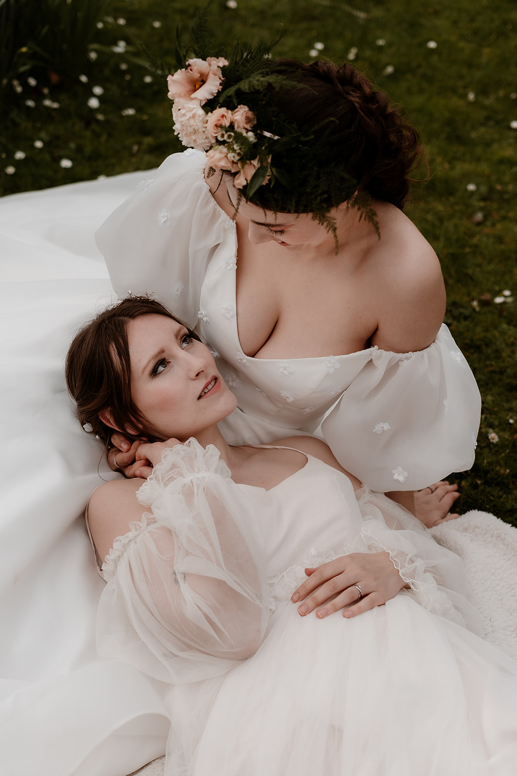 two brides sit and snuggle together on the grounds of Mapledurham House wedding venue in the spring sunshine