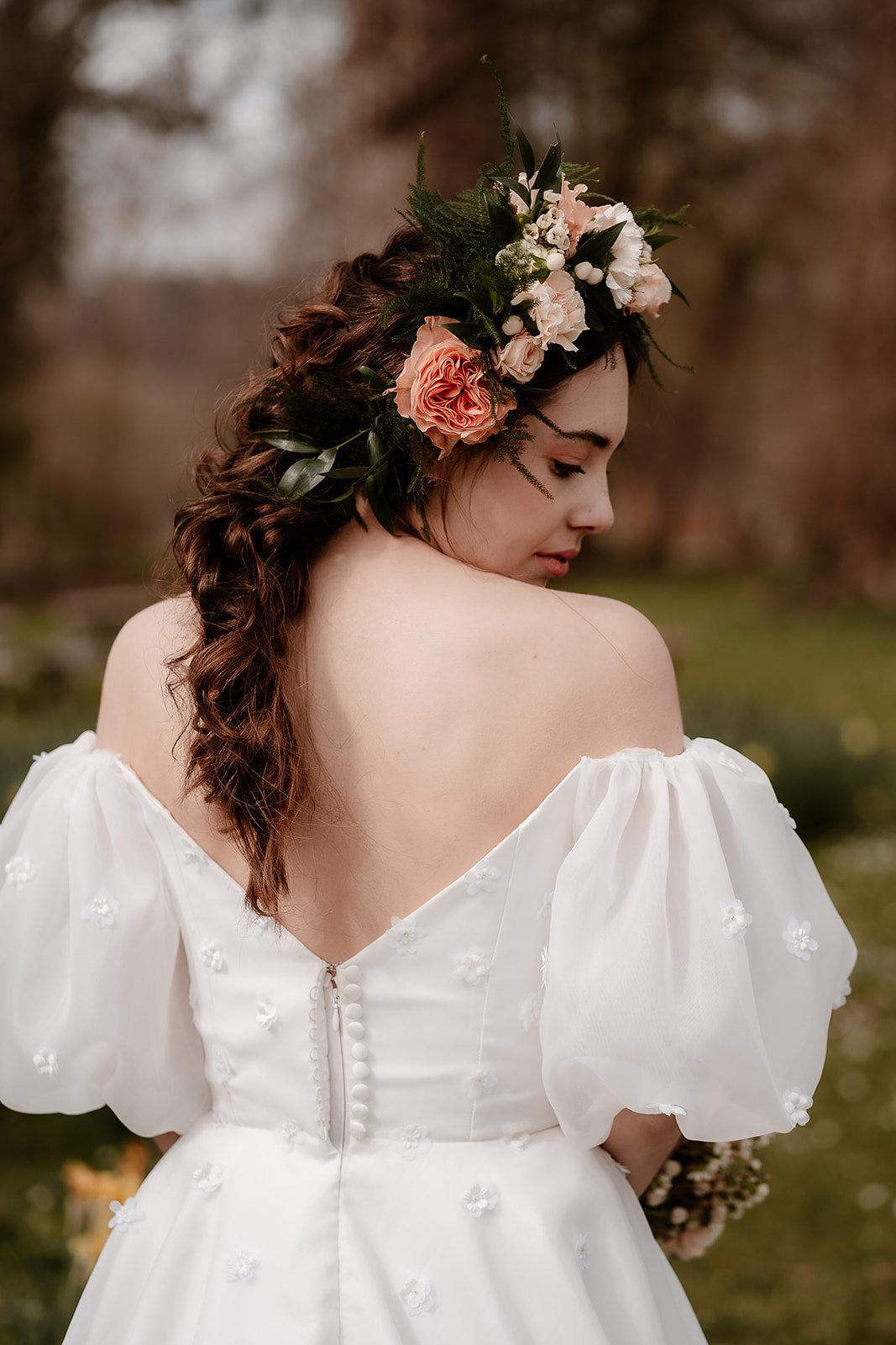 A bride wearing a flower crown looks down at her dress's puff sleeves while her soft braid falls down her back