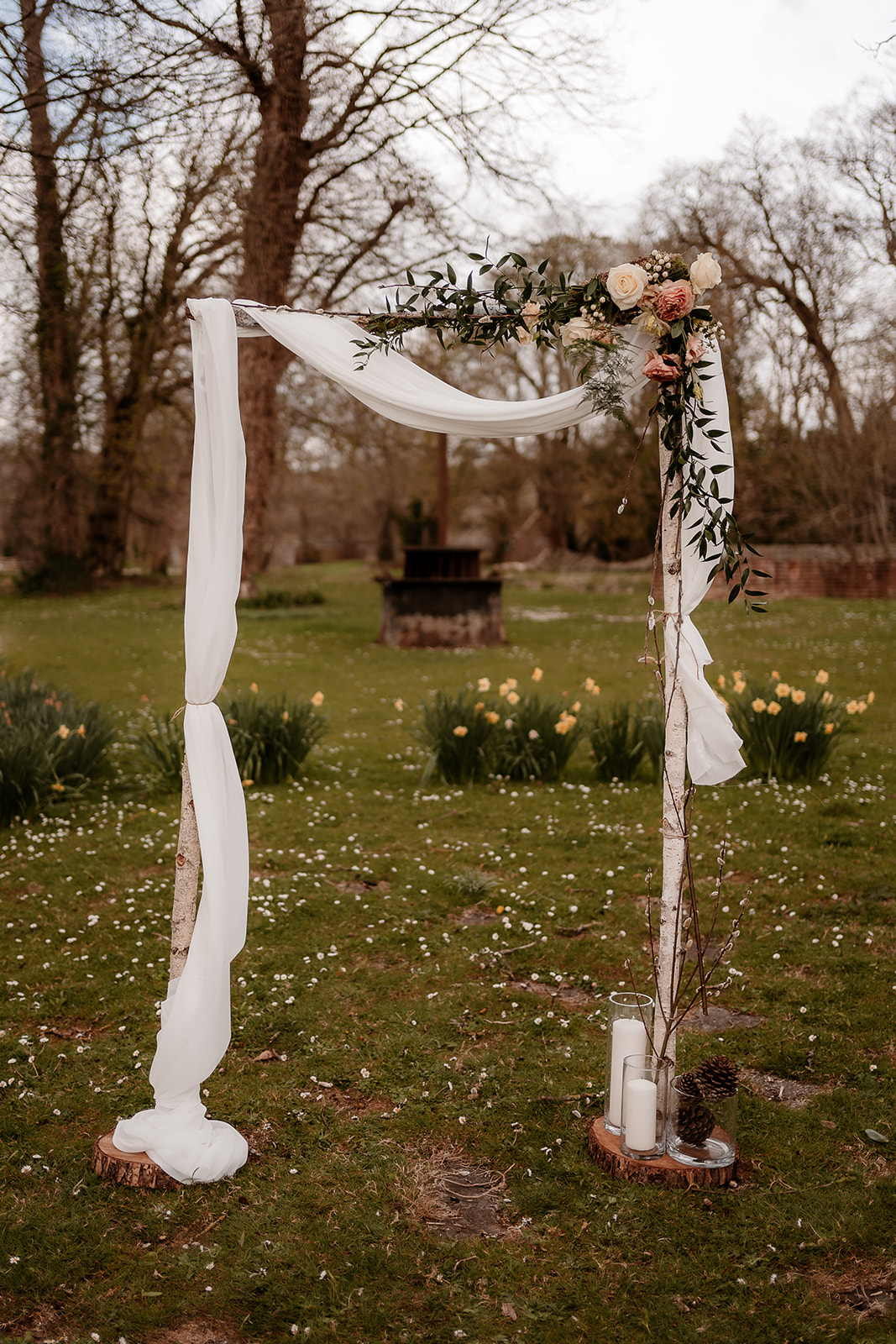 Birch ceremony arch at Mapledurham House with chiffon draping and peachy toned flower accents. 