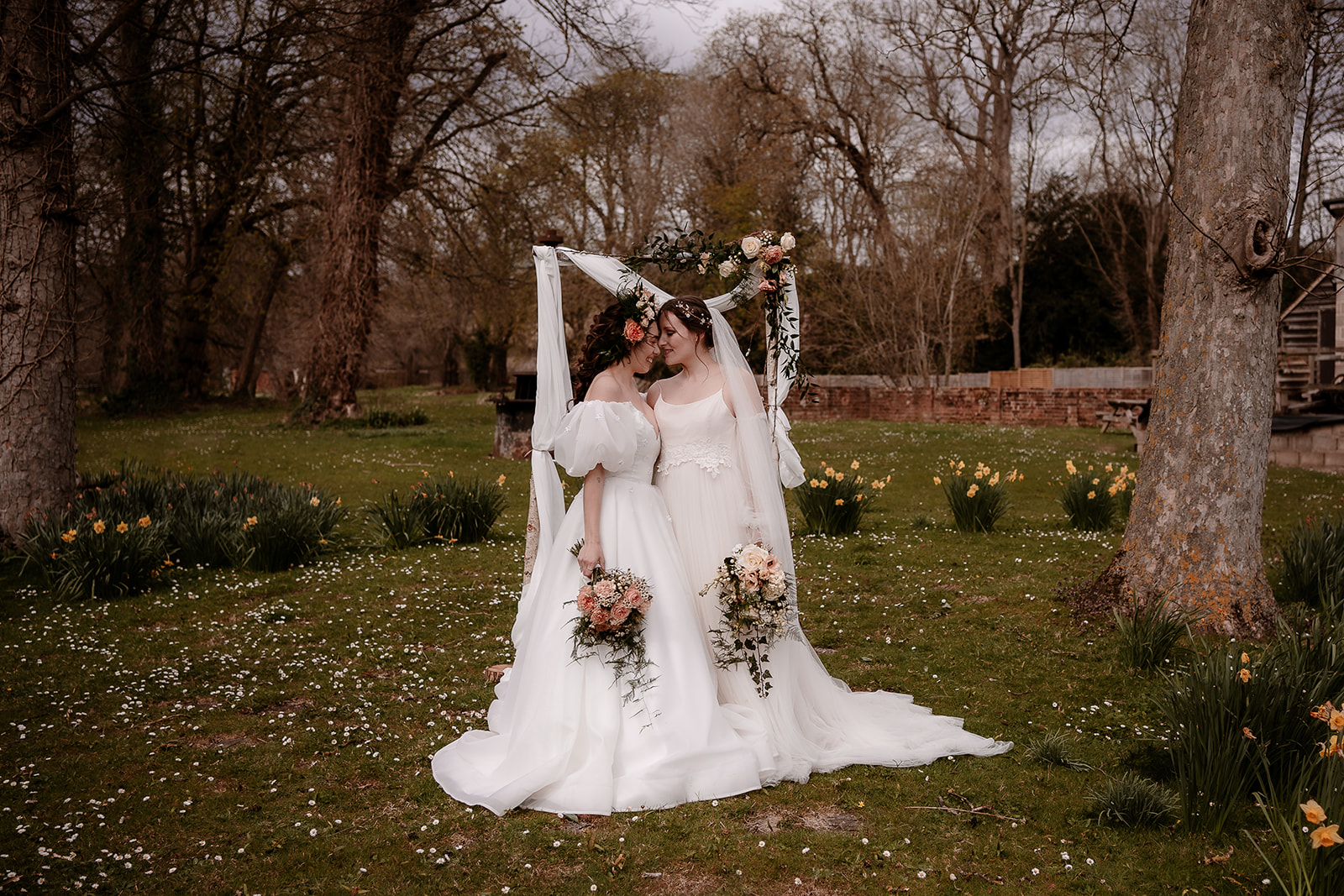 two brides stand together at their birch ceremony arch at Mapledurham House wedding venue