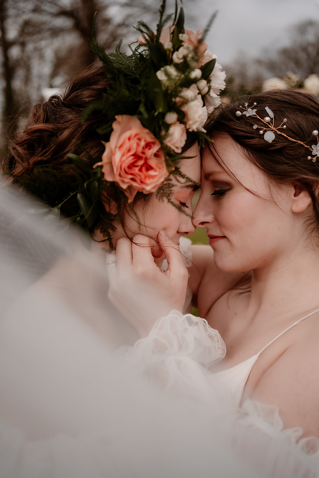 Two brides snuggle together with their heads close under a veil at their Mapledurham House wedding