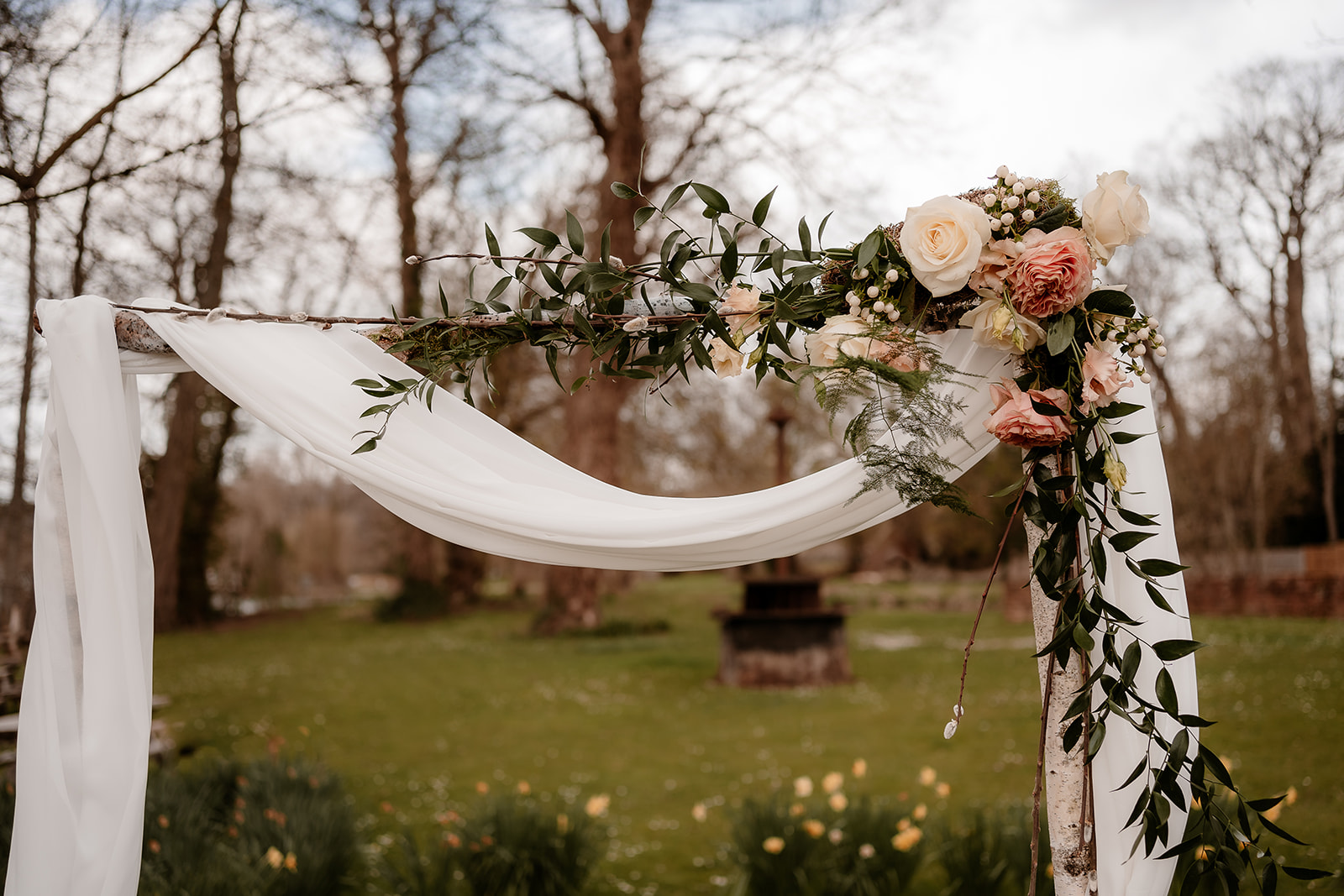 Close up shot of the birch ceremony arch at Mapledurham House with chiffon draping and peachy toned flower accents. 