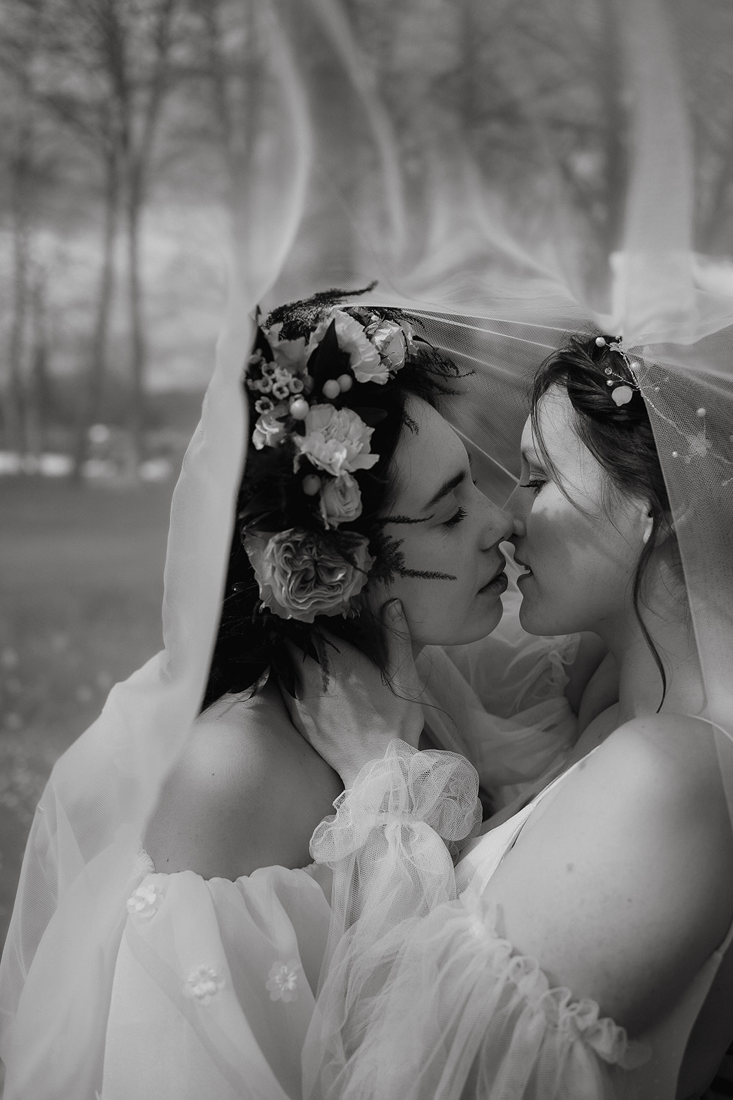 Two brides snuggle together with their heads close under a veil at their Mapledurham House wedding