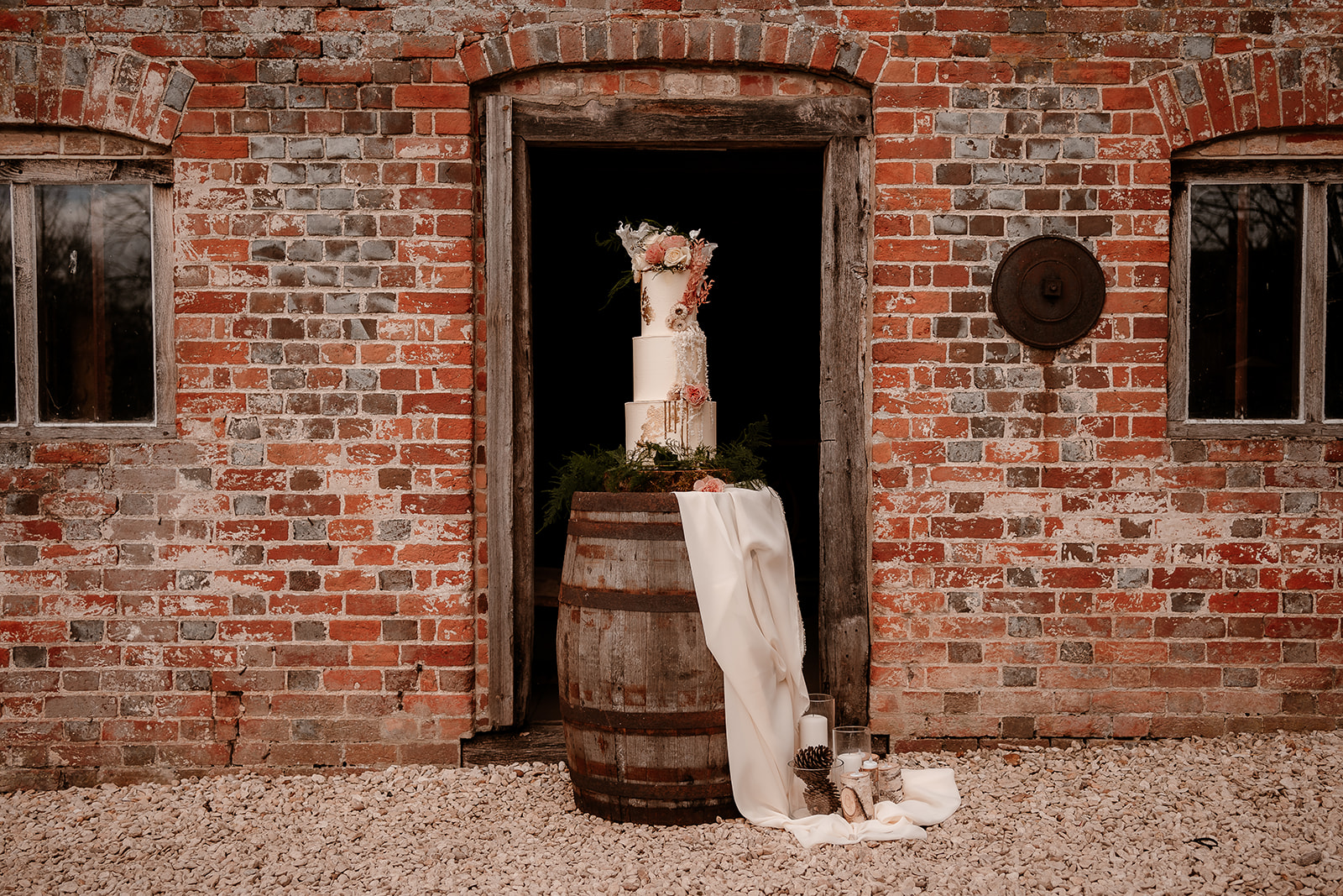 Stunning wedding cake sits on a wooden barrel framed by the door of Mapledurham water mill