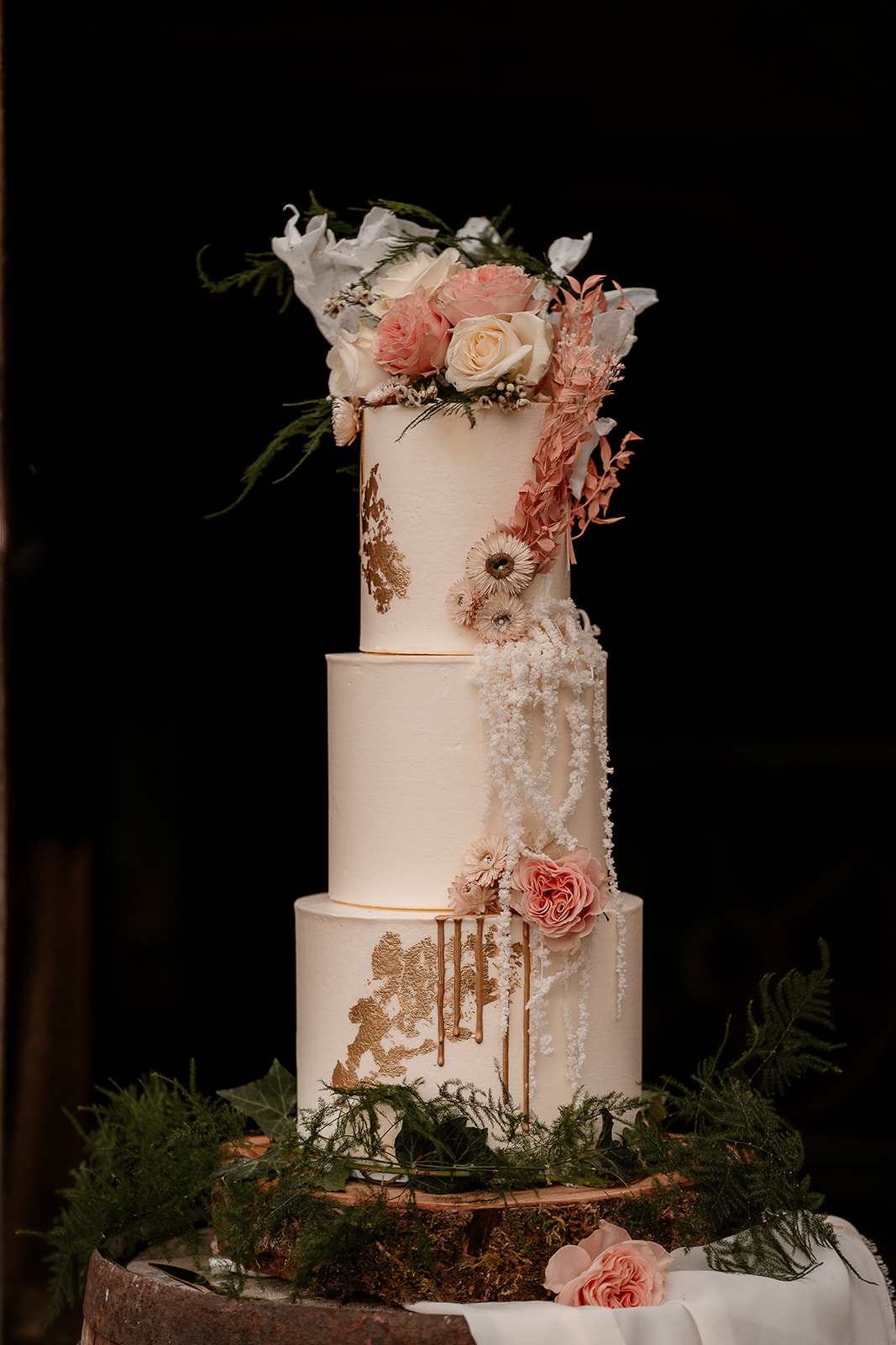 Three tier wedding cake in peachy tones with gold leaf decoration and floral topper