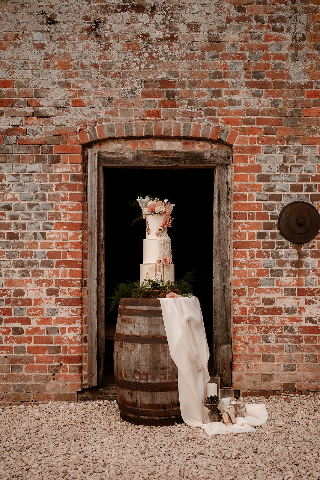 Stunning wedding cake sits on a wooden barrel framed by the door of Mapledurham water mill