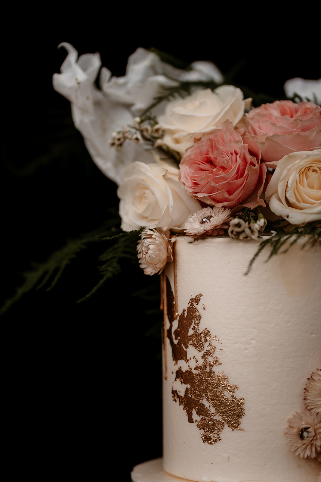 close up of a Three tier wedding cake in peachy tones with gold leaf decoration and floral topper
