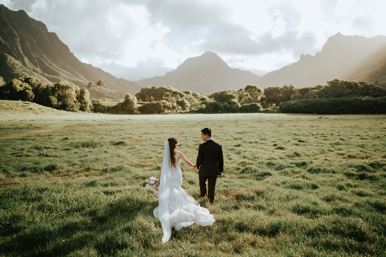 Newlyweds strolling in sunny field in Kualoa Ranch
