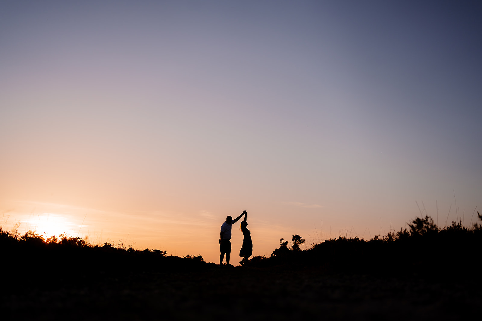 Silhouette of a couple dancing together in front of a sunset just dipping behind the horizon. 
