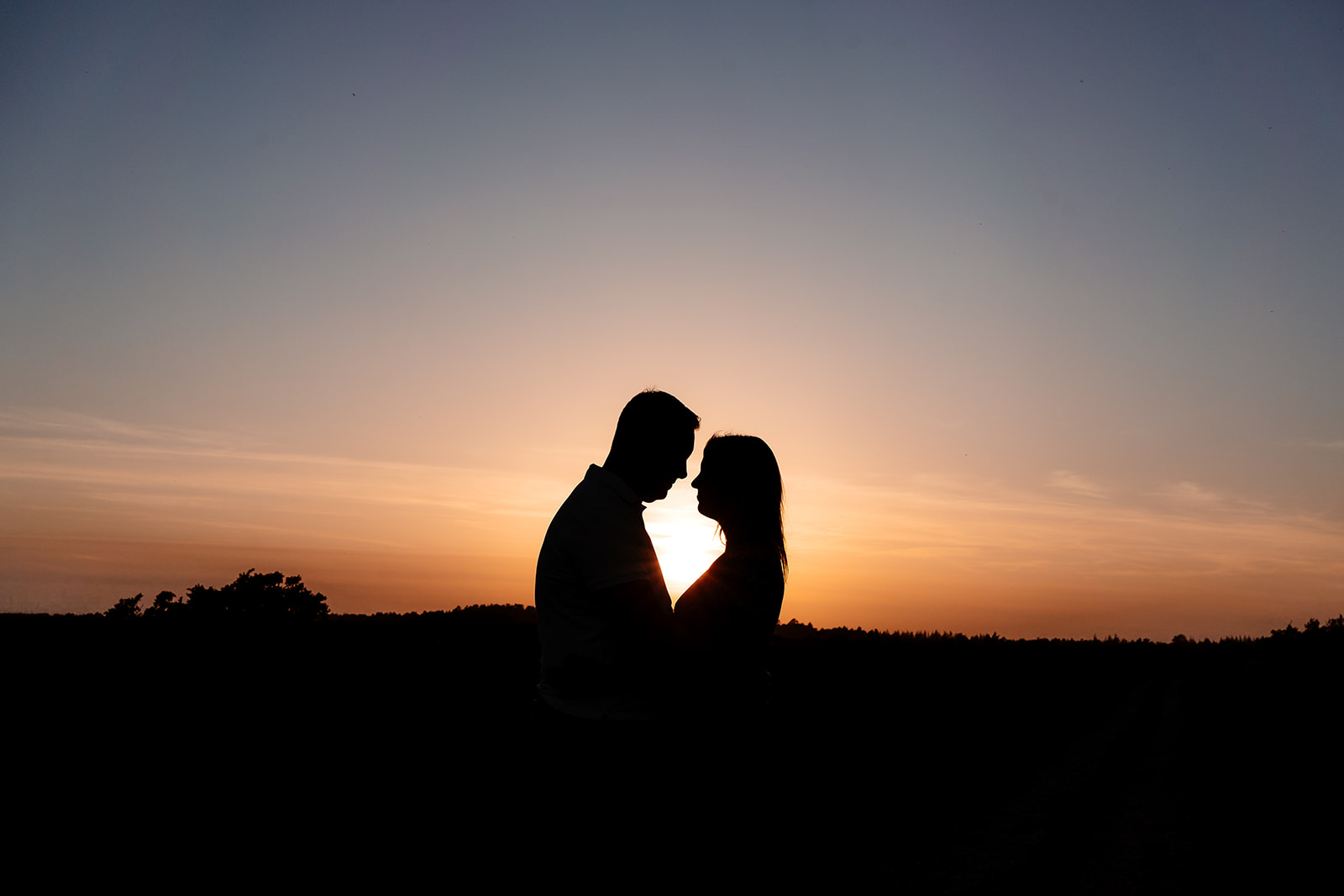 A newly engaged couple stand nose to nose in silhouette against the sunset. 