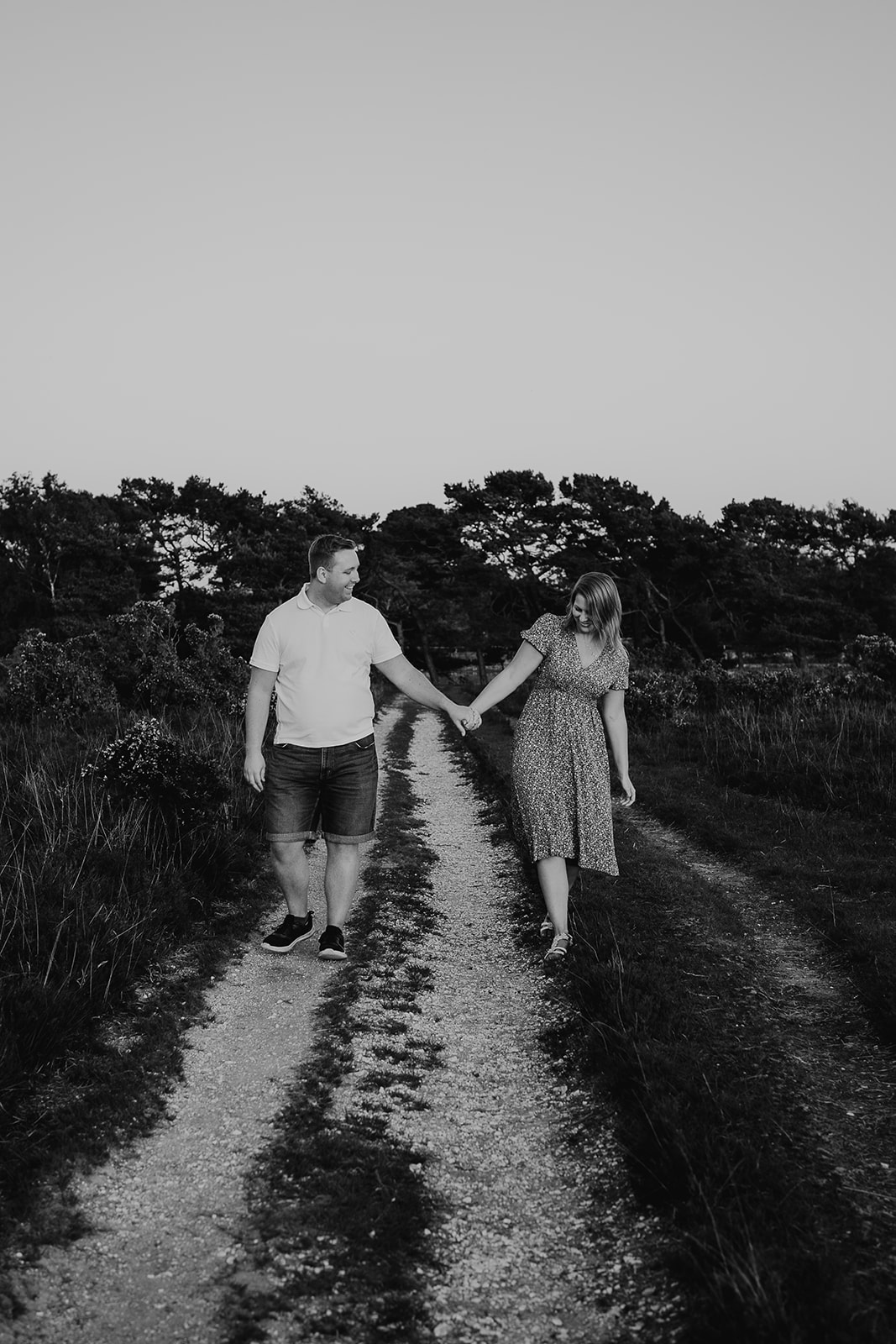 Black and white photo of a newly engaged couple walking hand in hand and laughing together. 