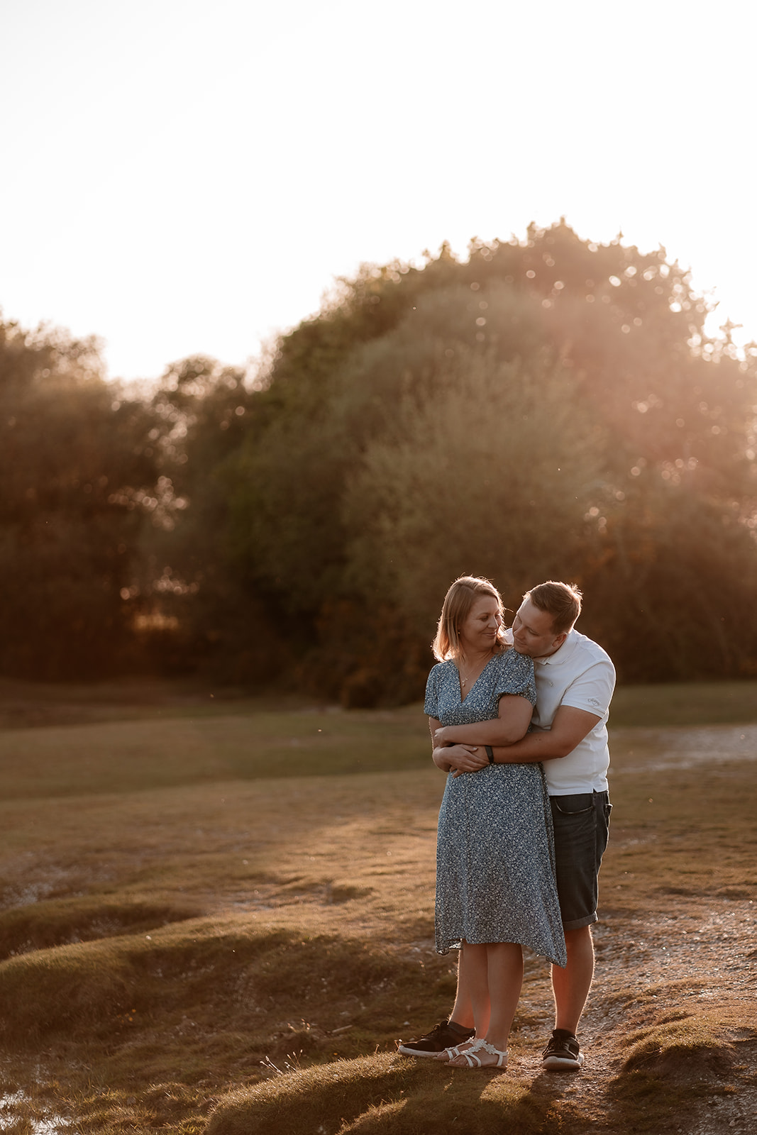 An engagement photoshoot in the New Forest. The couple cuddle together in the golden light of sunset. 
