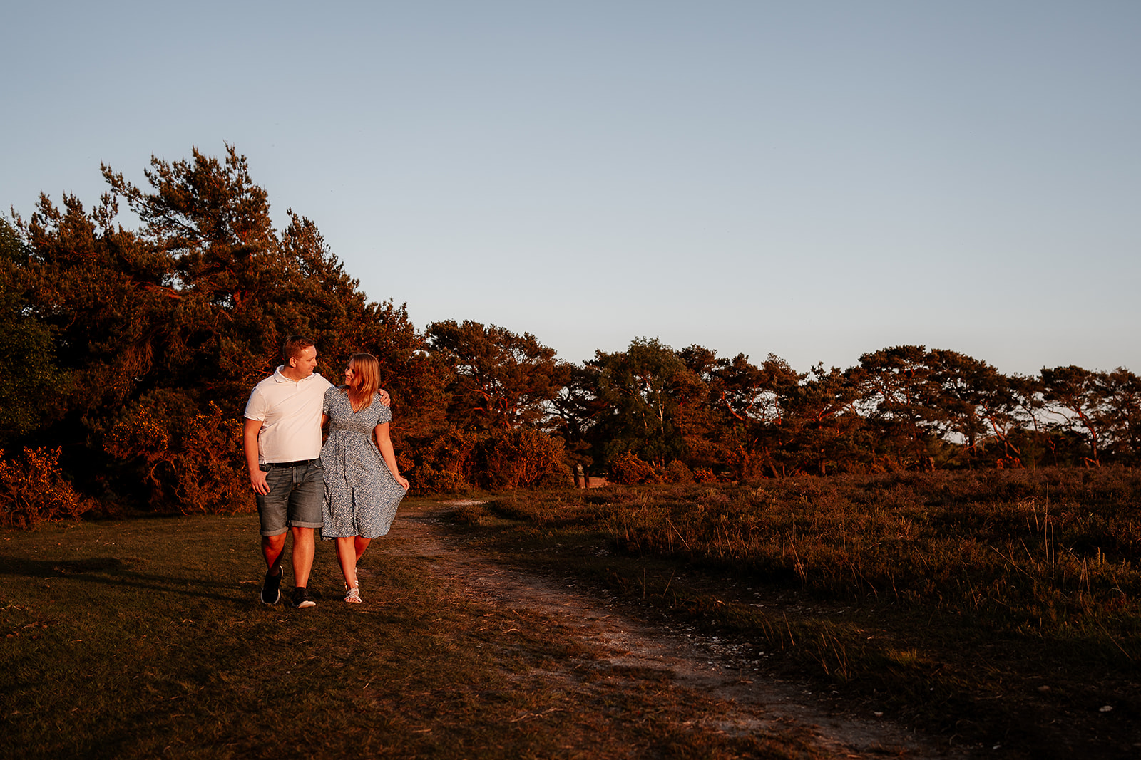A newly engaged couple walks hand in hand in the New Forest at golden hour. 