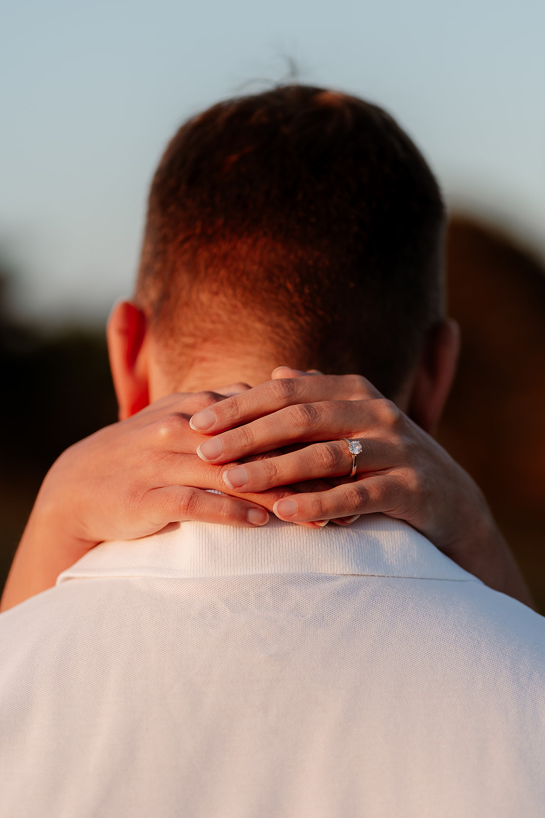 A woman wraps her hands around her husband's neck in an embrace to show off her engagement ring