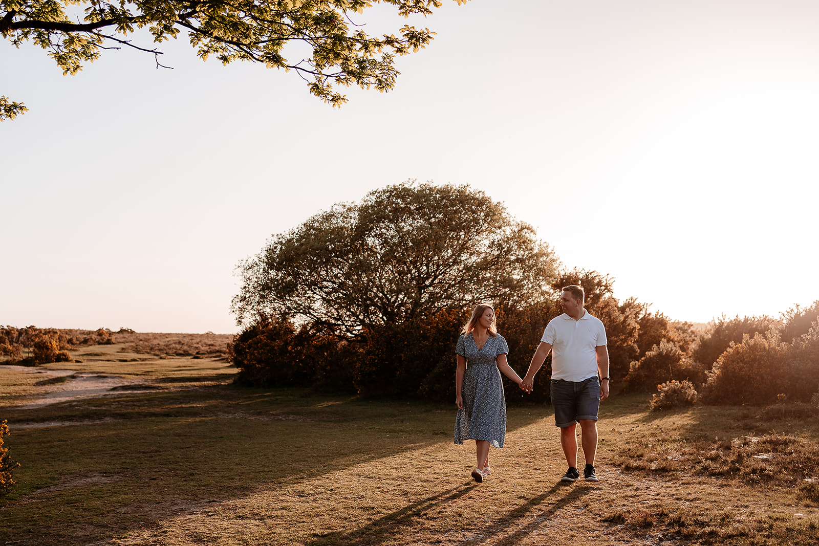 A newly engaged couple walks hand in hand in the New Forest at golden hour. 