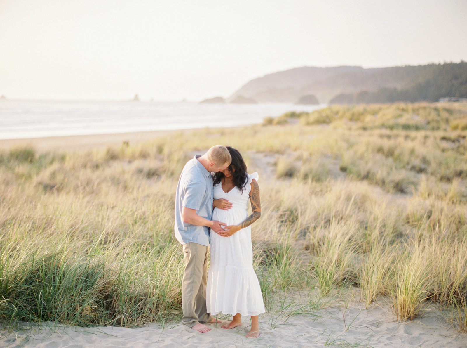a couple embraces at Cannon Beach as they anticipate their first child
