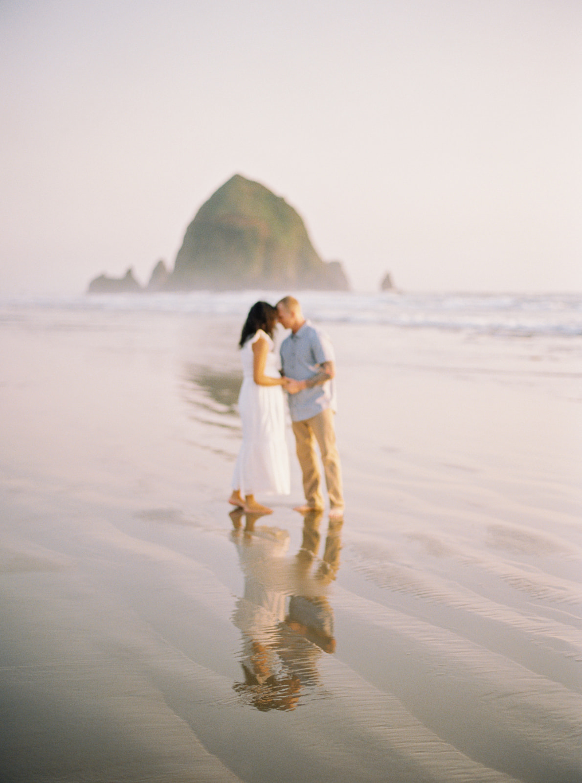 an expectant couple poses in front of Haystack Rock on the Oregon coast, on medium format film
