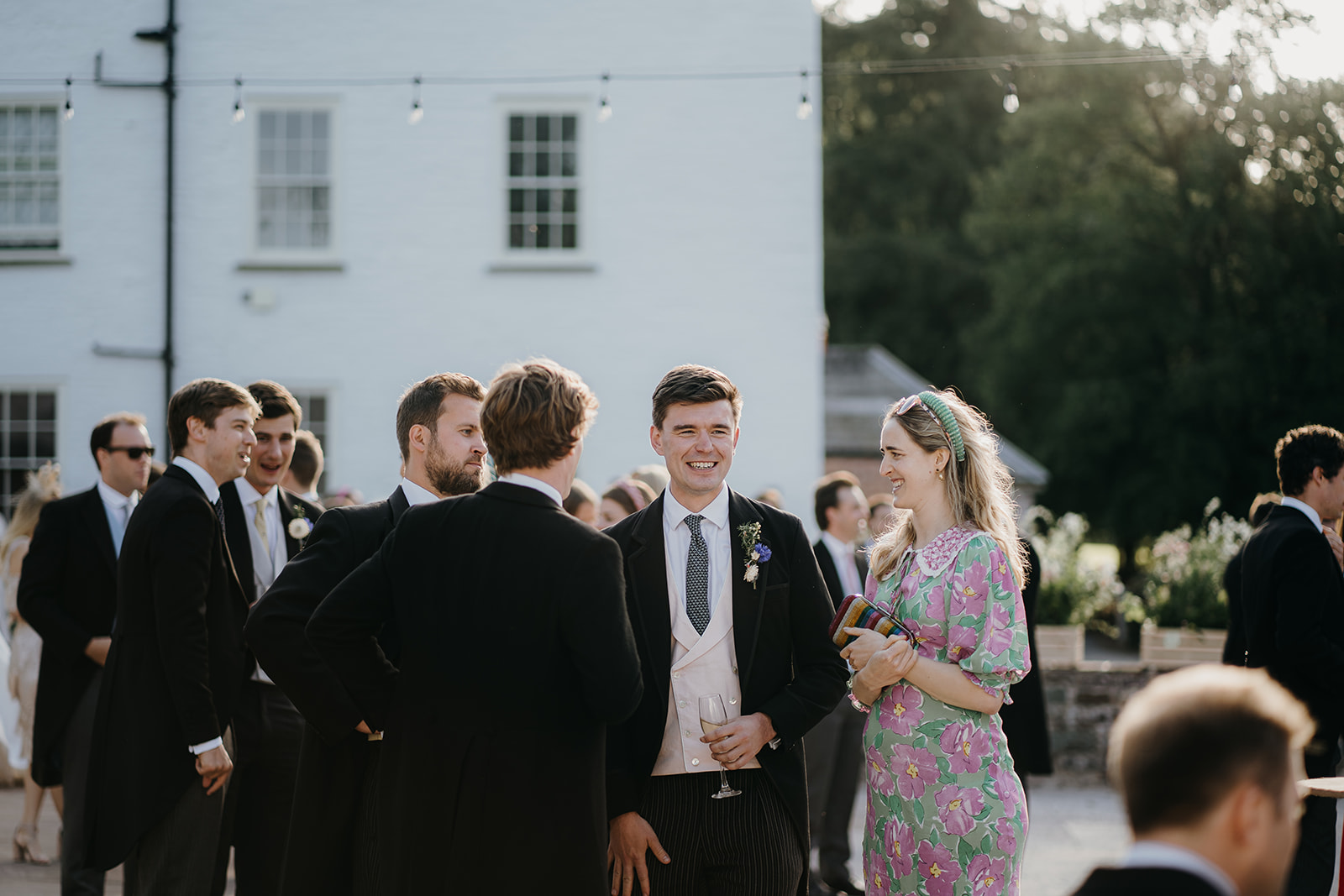 Natural candid moment of the groom talking with guests in the evening sunlight.