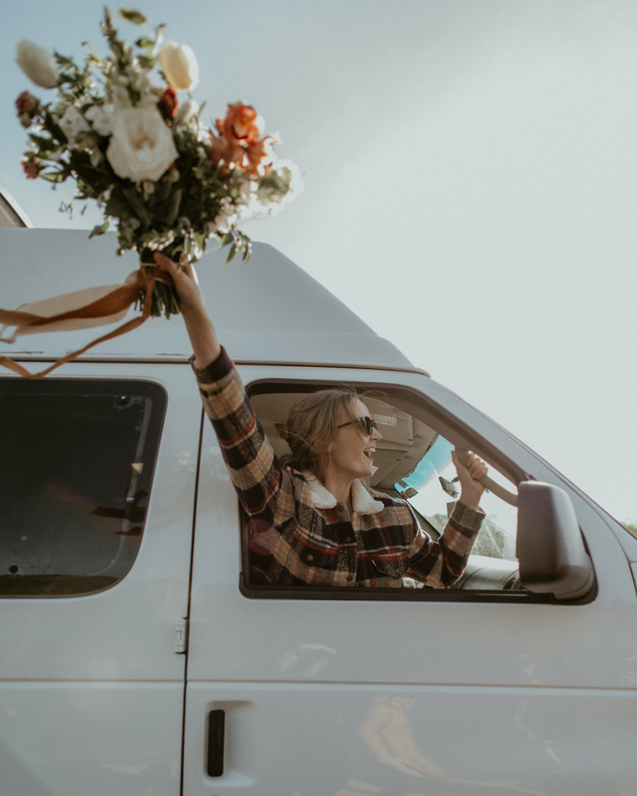 Bride waves bouquet out window of van during white mountains elopement