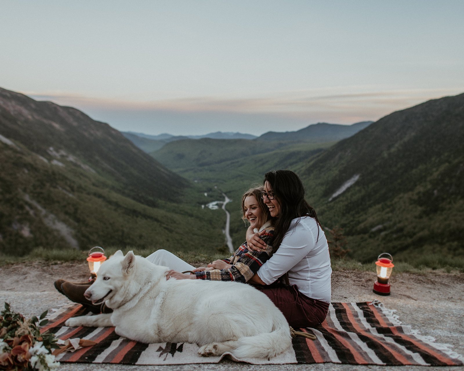 Couple sits together with their dog on blanket overlooking Crawford Notch for their White Mountains Adventure Elopement