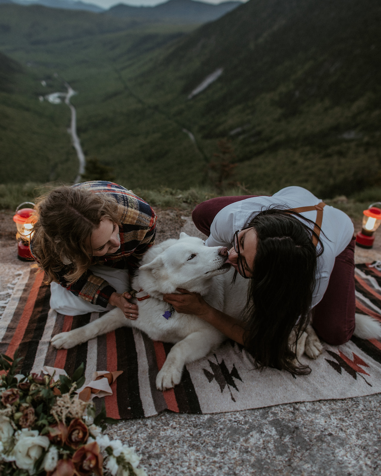 Couple sits together with their dog on blanket overlooking Crawford Notch for their White Mountains Adventure Elopement
