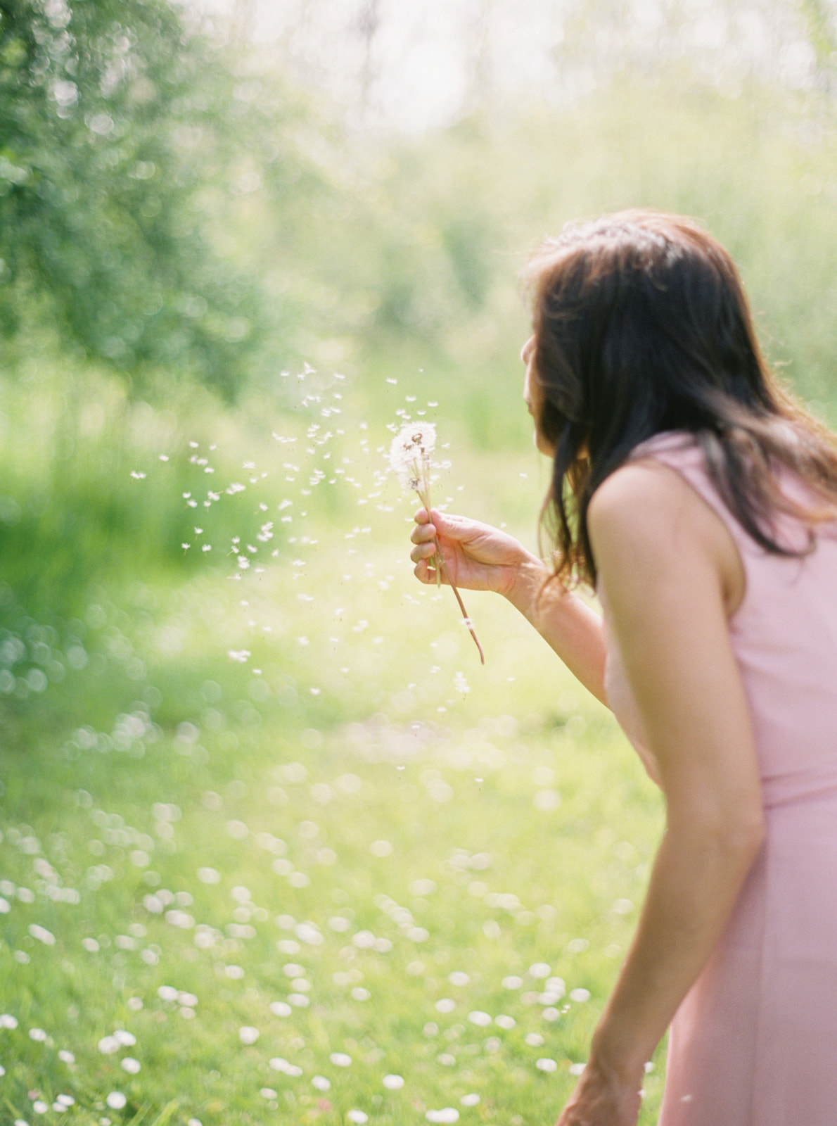 a woman in a pink dress makes a wish with a dandelion