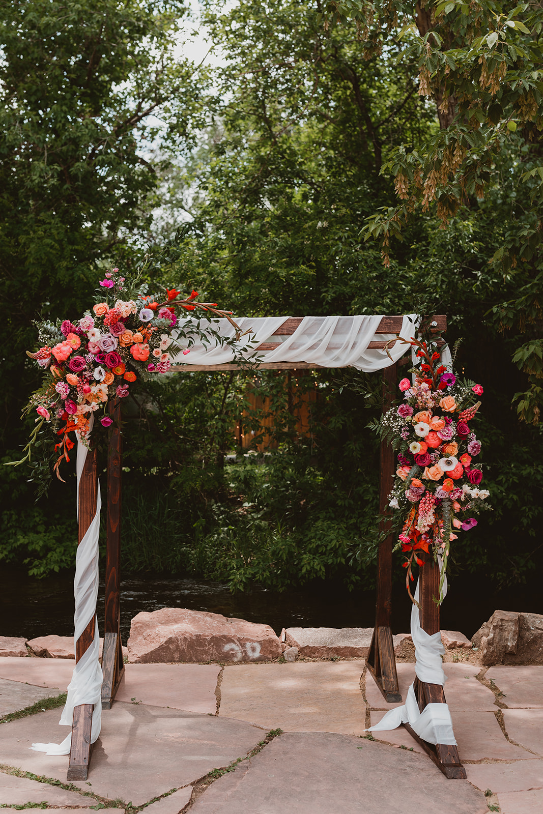 Stunning wooden arch adorned with white fabric and bright pink flowers in Denver Colorado at Lyons Farmette