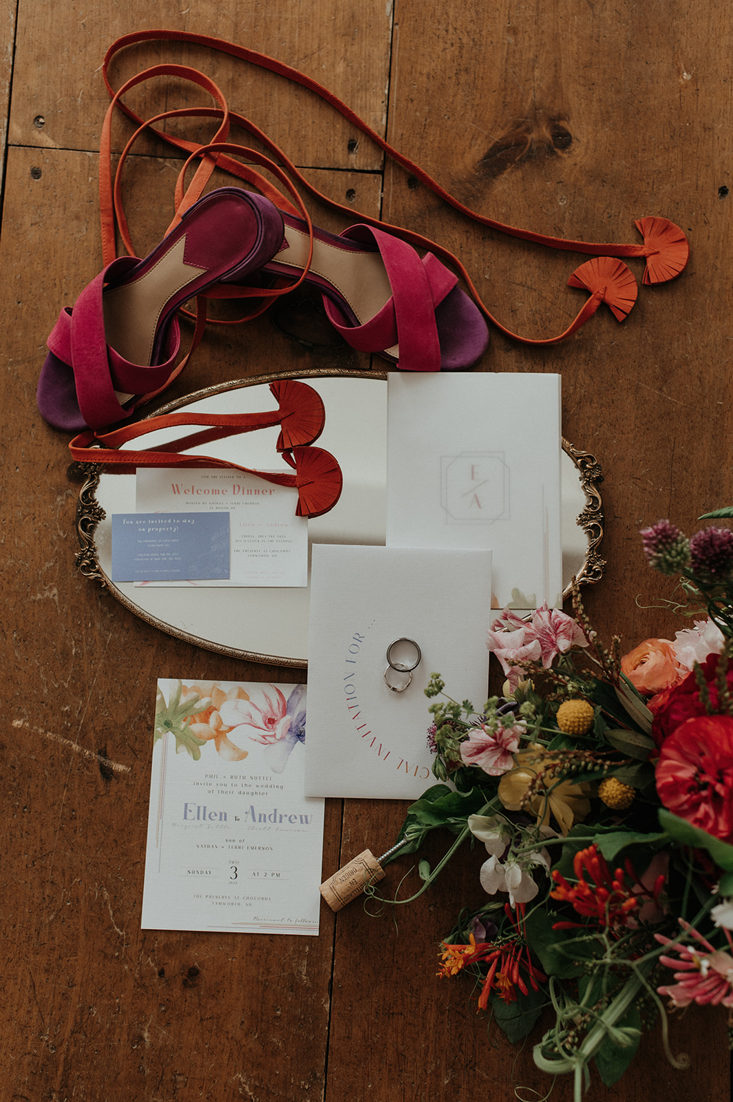 Flat lay of bridal details with invitation florals and wedding rings