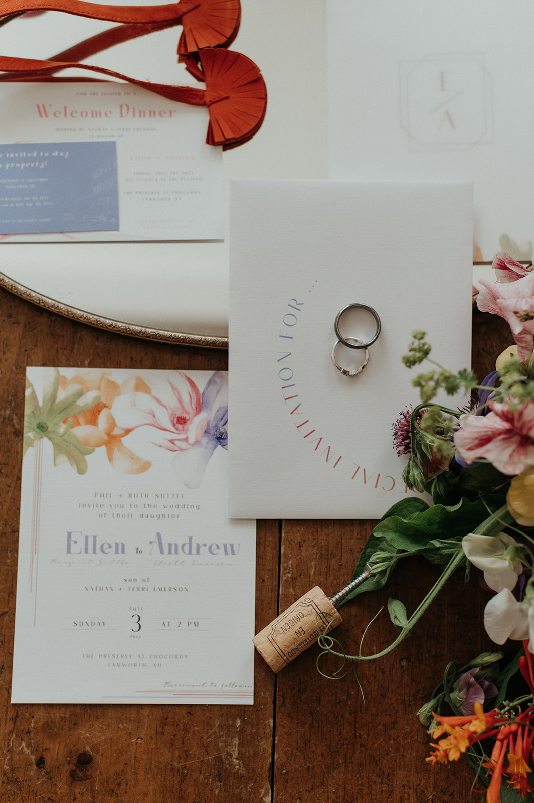 Flat lay of bridal details with invitation florals and wedding rings
