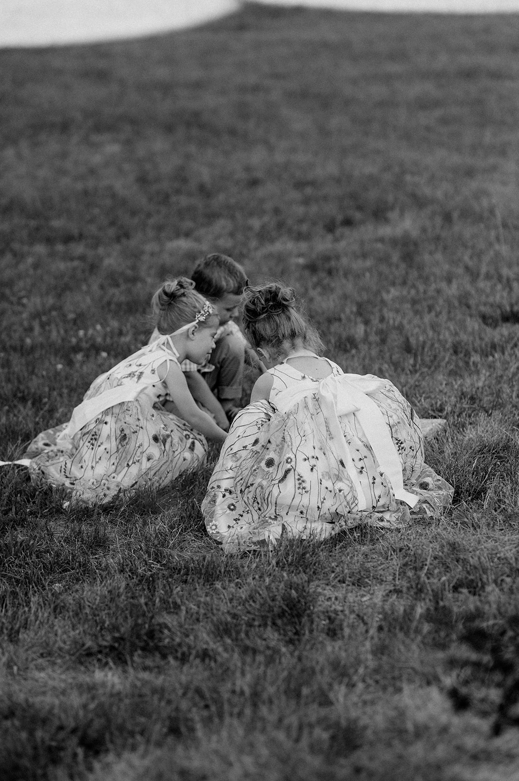 black and white candid photo of flower girls playing in the dirt