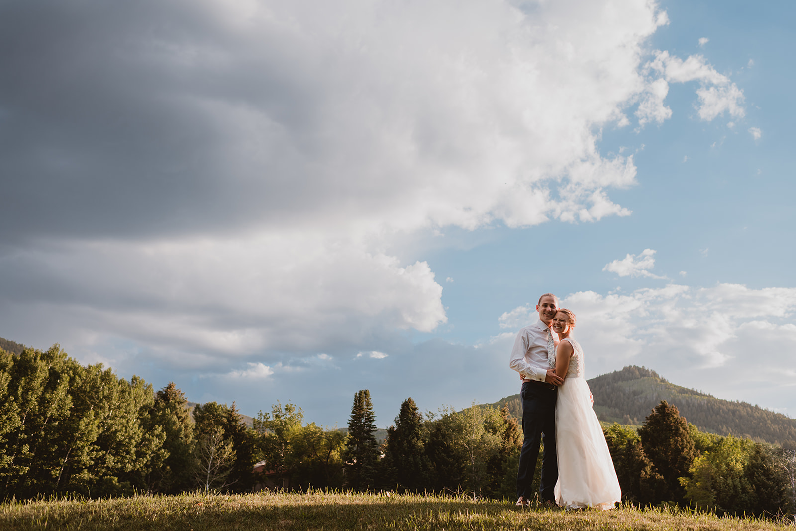 Couple stands below mountains in their wedding attire in Vail, Colorado 