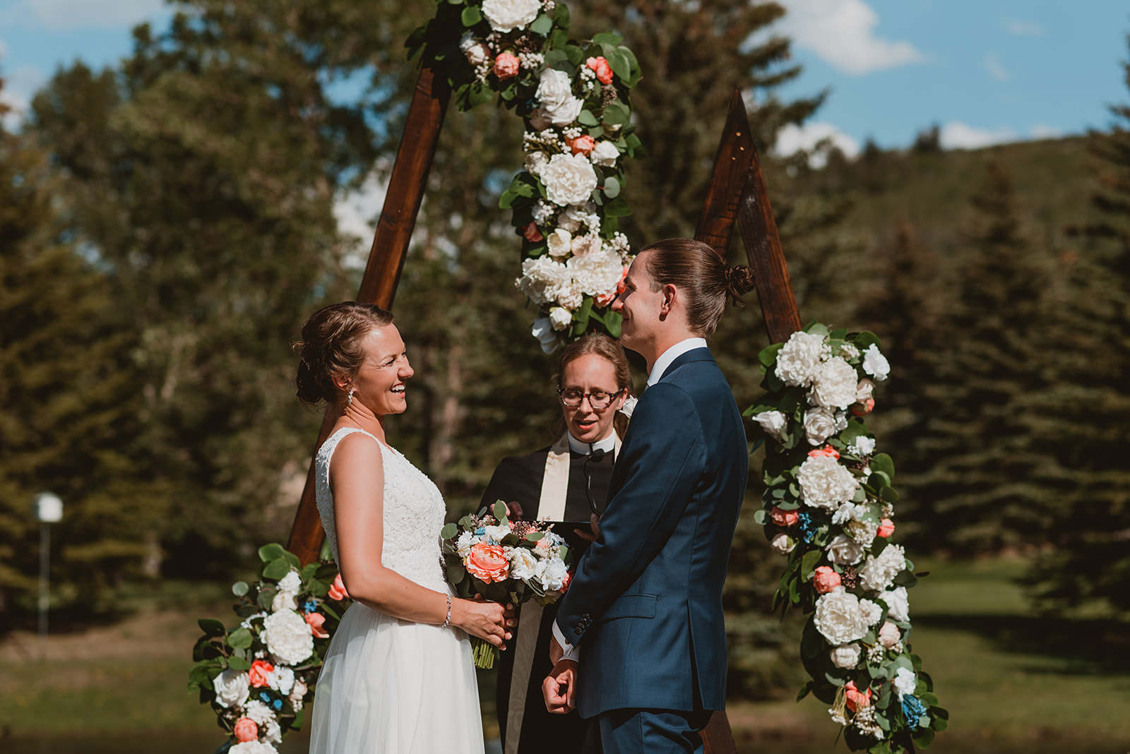 Couple stands in front of arch covered in flowers on their wedding day in Vail, CO