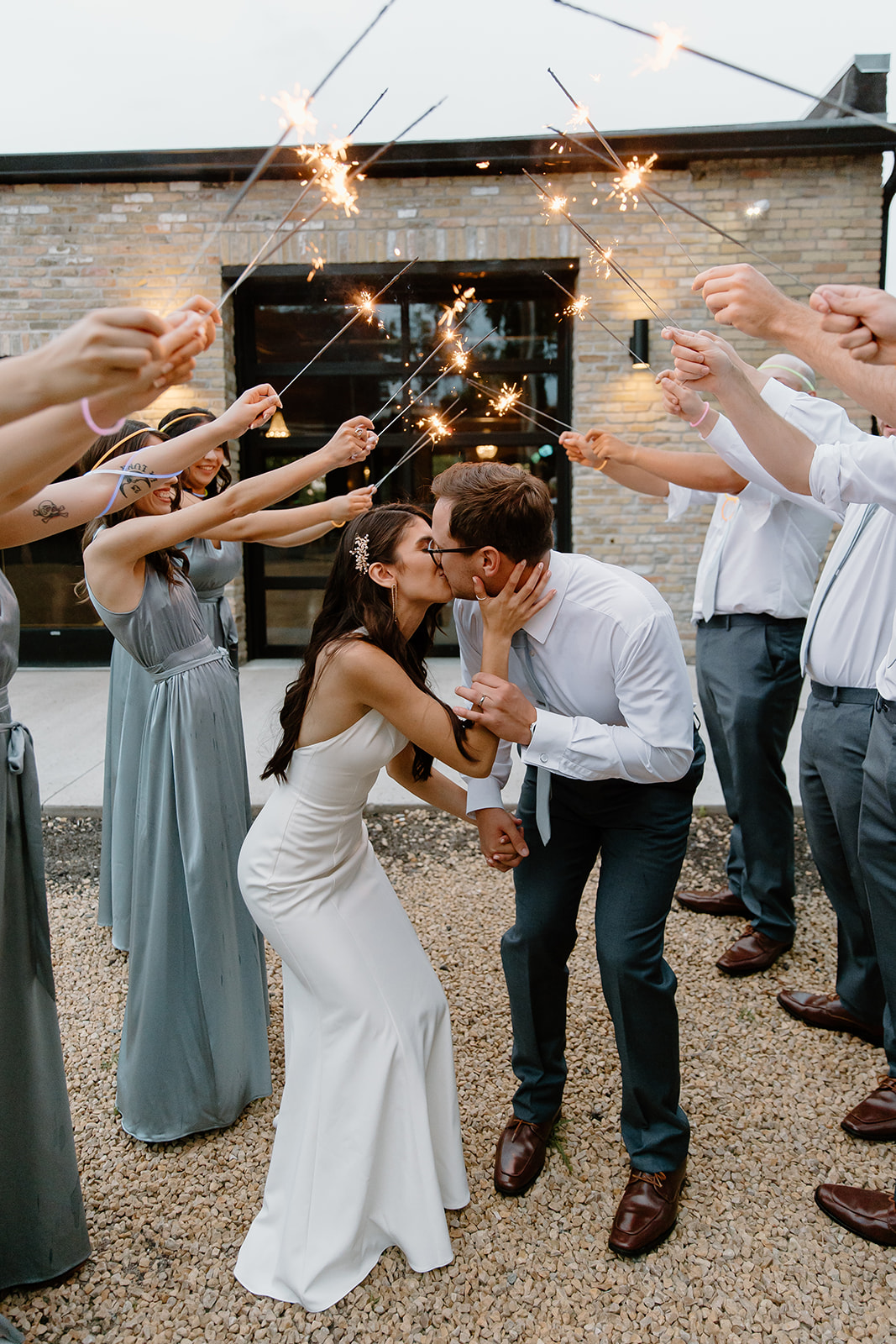 Bride and groom run through sparklers while kissing