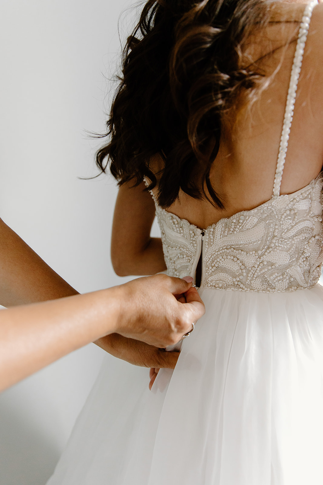 A mother's hands zip her daughter's wedding dress