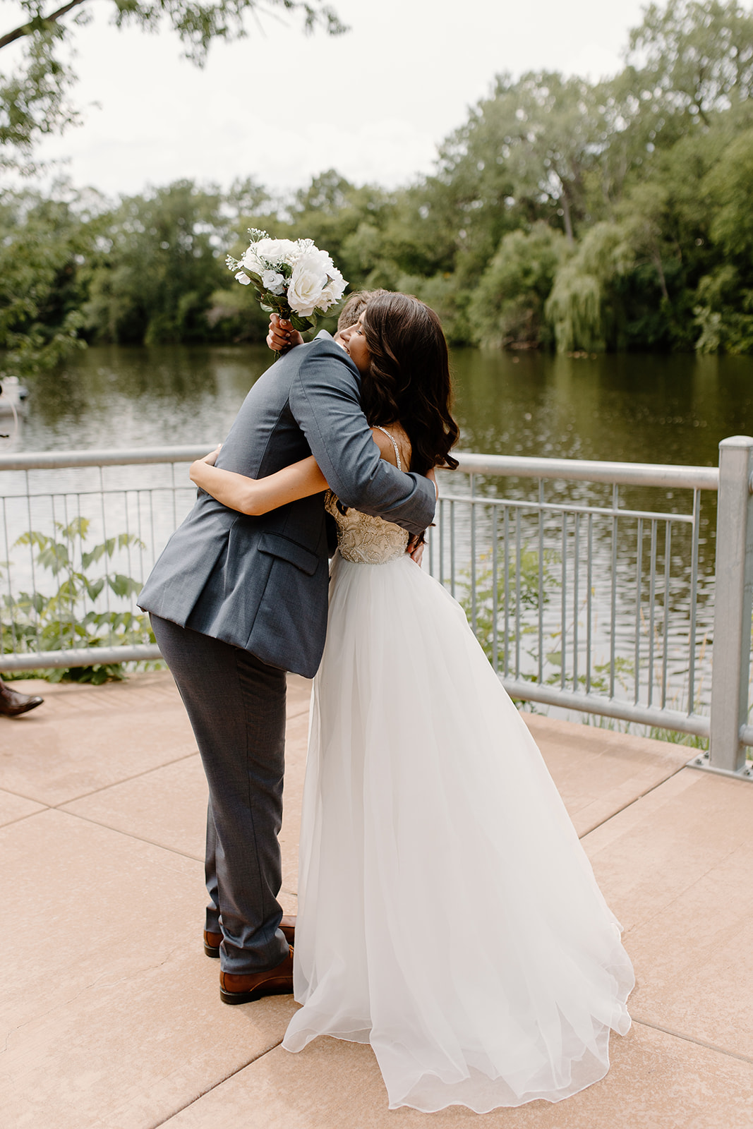 Bride and groom share a hug in front of a river