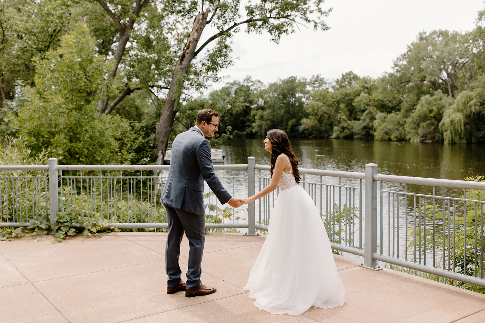 Bride and groom laugh at each other in front of a river