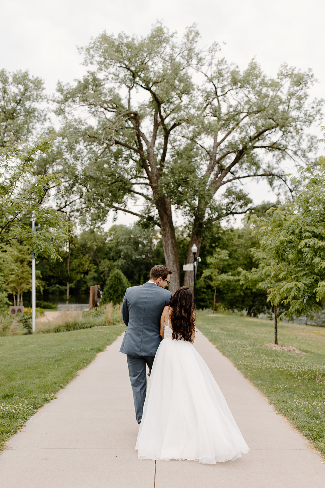Bride and groom walk away towards a tree