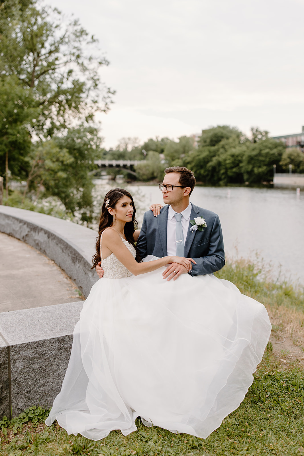 Bride and groom sit down in front of a river