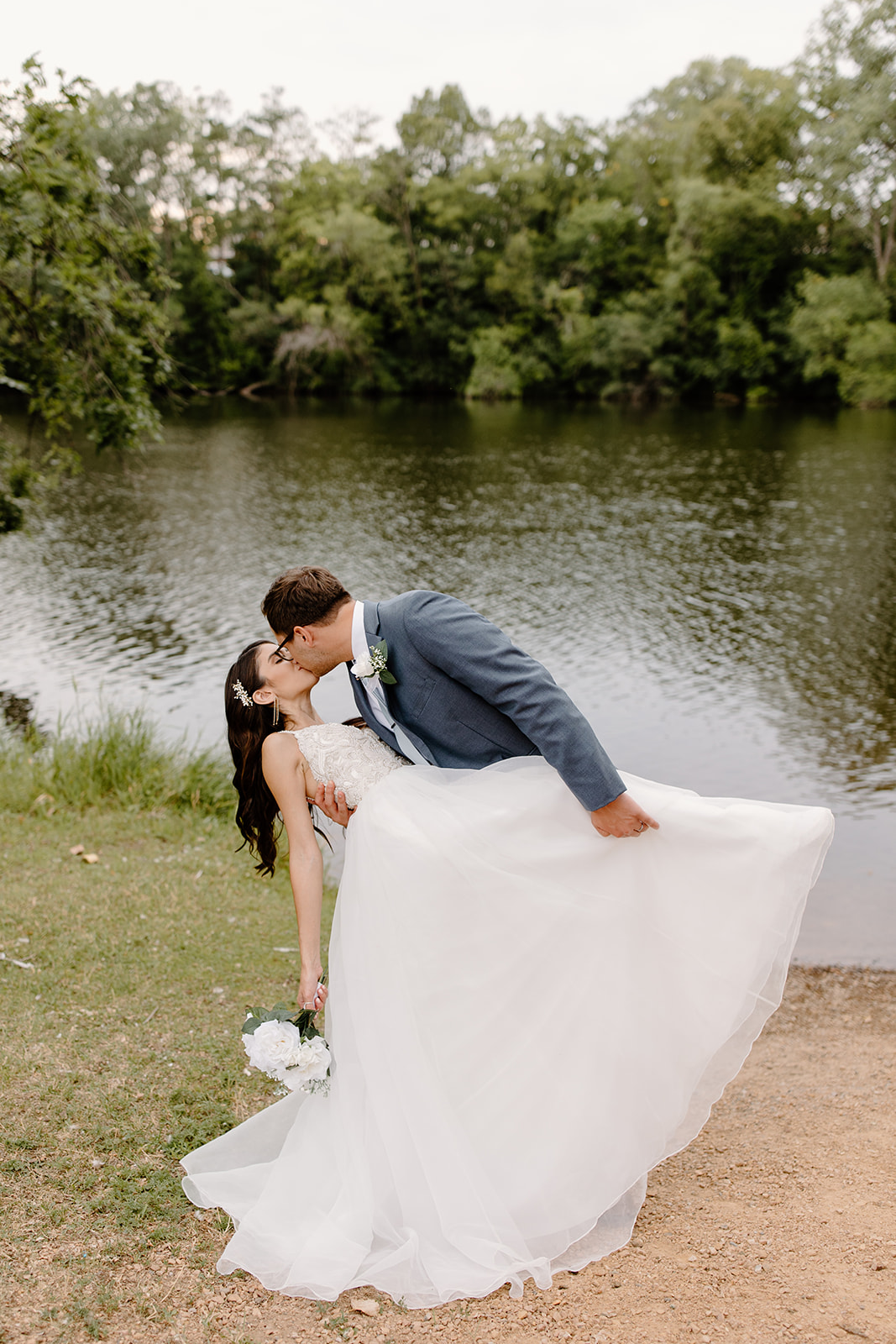 Groom dips his bride for a kiss in front of a river