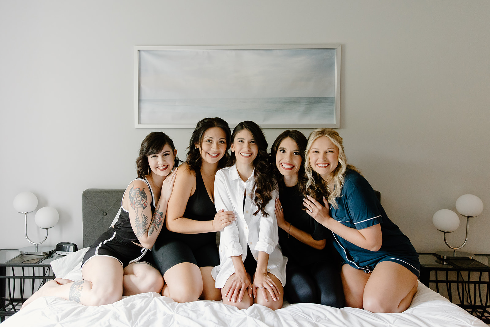 Bride and her friends smiling while sitting on a bed