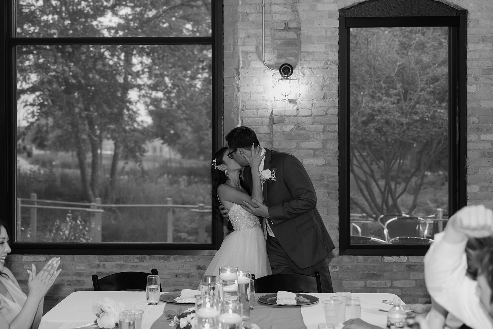 Groom and bride stand up next to their dinner table and share a kiss
