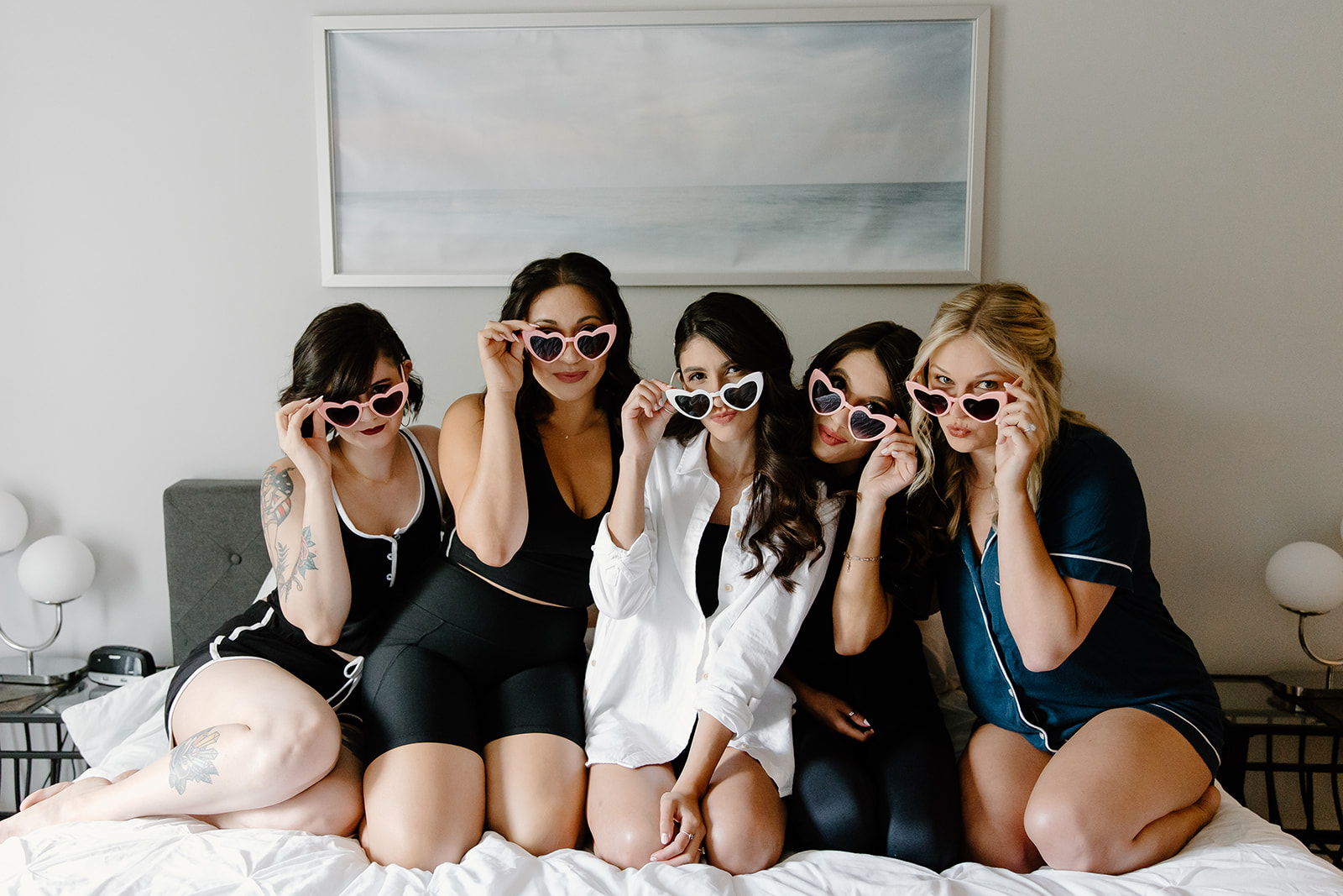 Bride and her friends wearing sunglasses while sitting on a bed