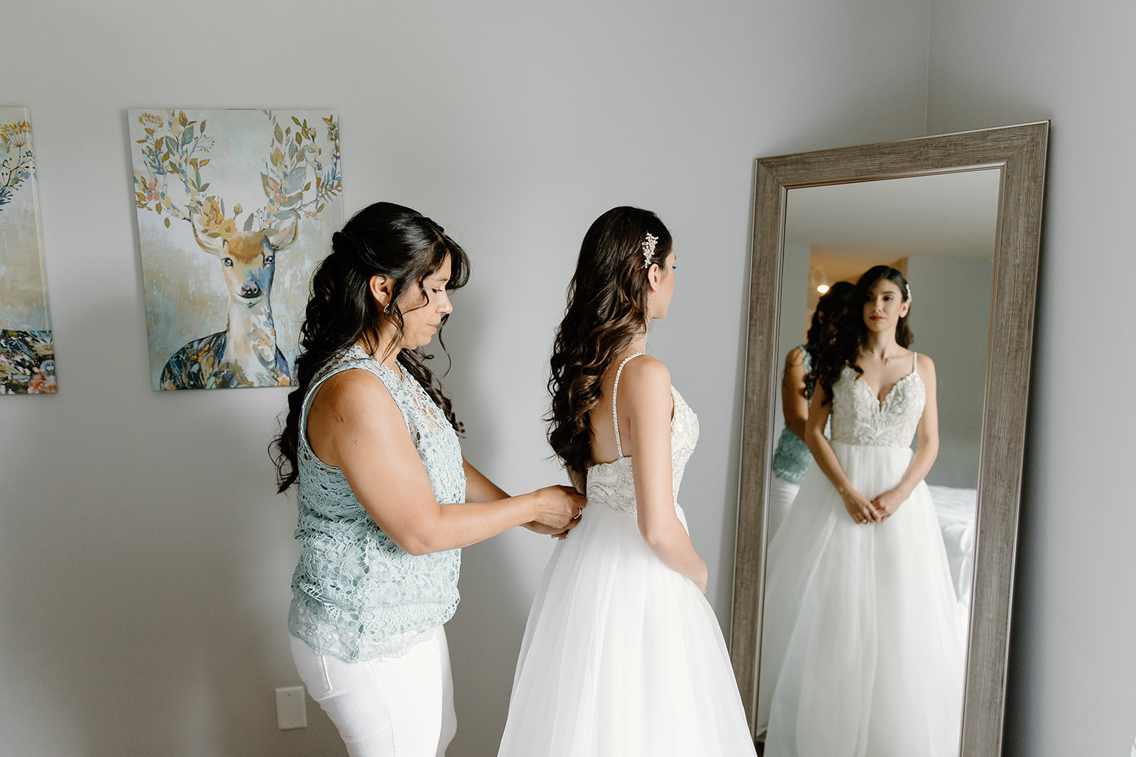 Mother zips her daughter's wedding dress in front of a mirror