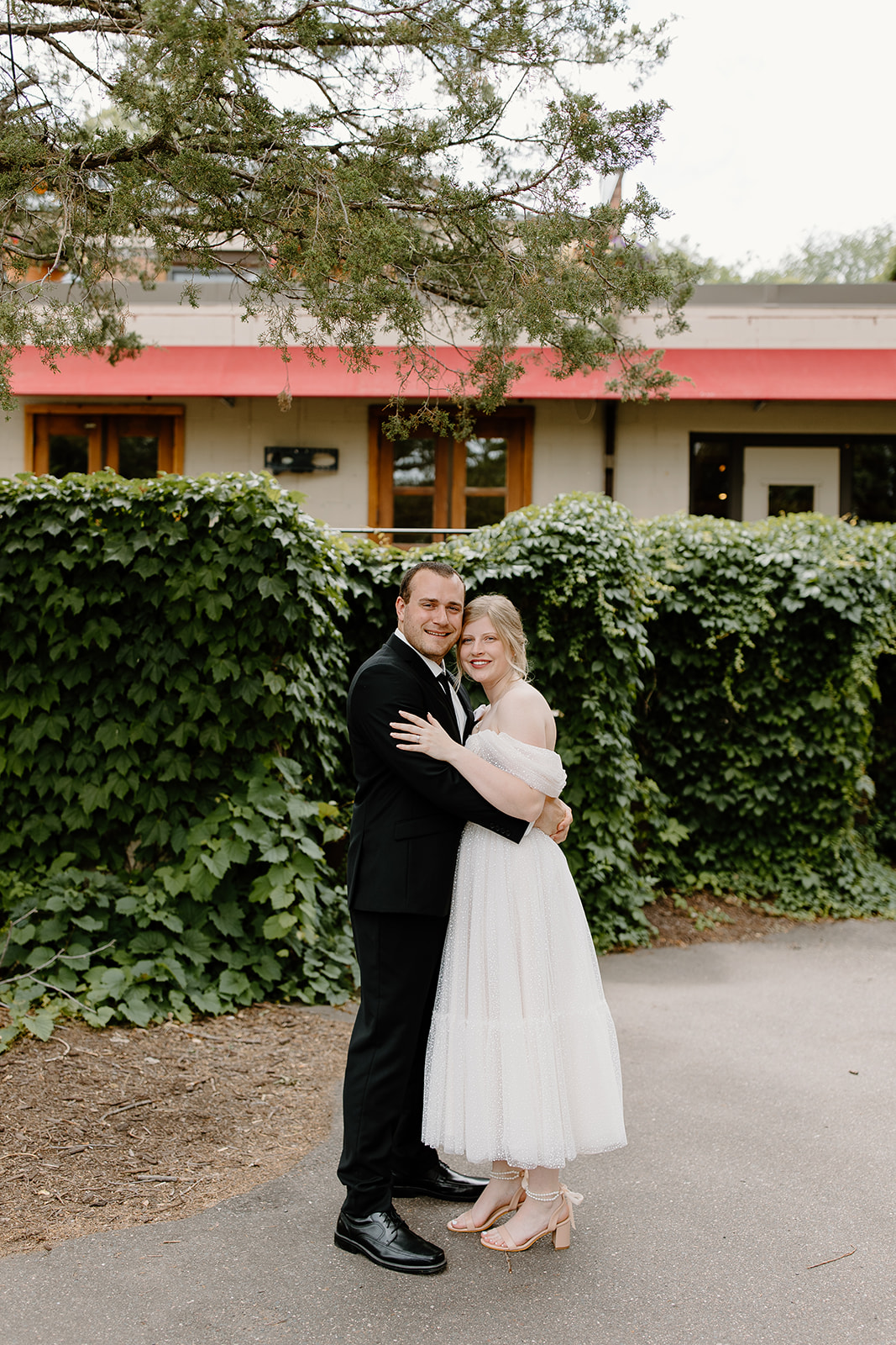 Bride and groom hold each other and smile in front of a wall of vines