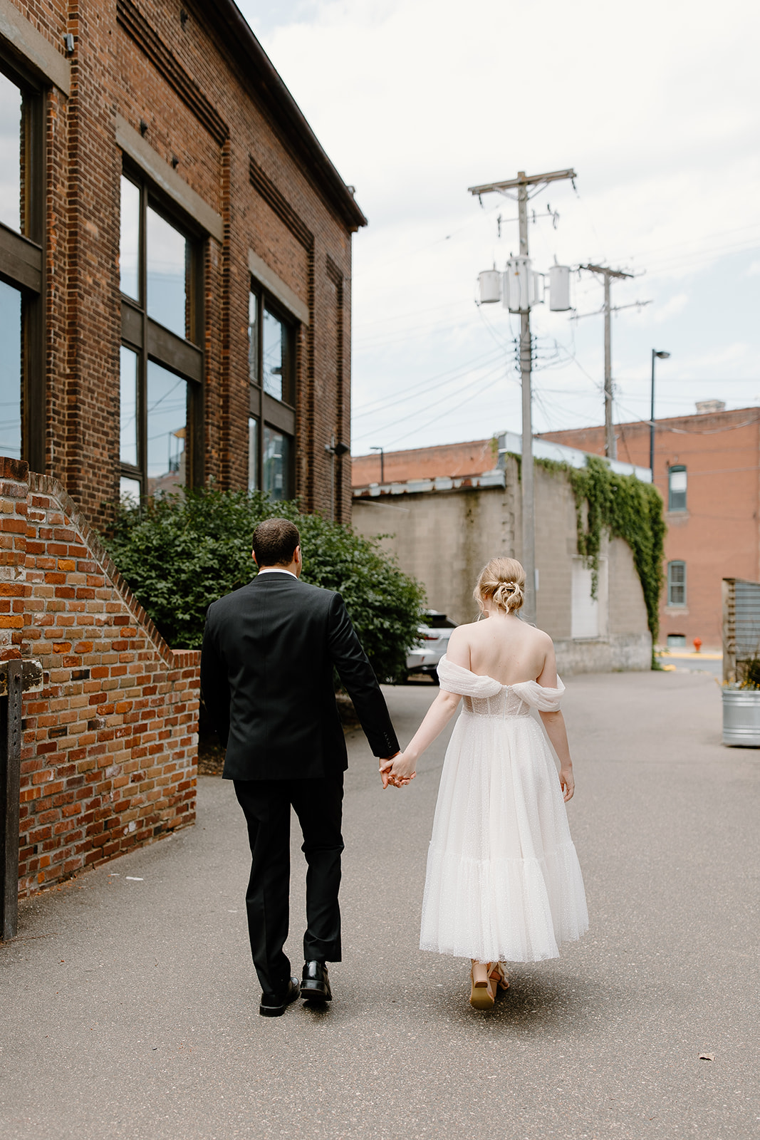 Bride and groom hold hands and walk through an alley